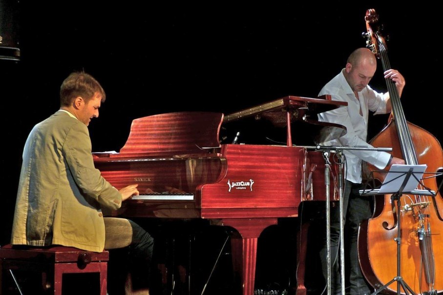 Ein Pianist spielt auf einem Fl&uuml;gel, w&auml;hrend ein Kontrabassist daneben steht. Beide Musiker sind in einem Jazzclub auf der B&uuml;hne., &copy; Foto Dieter Reinm&uuml;ller