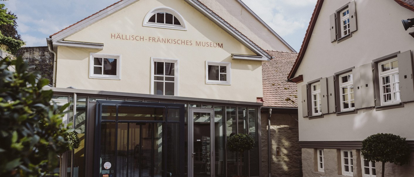 Eingang des Hällisch-Fränkischen Museums in Schwäbisch Hall, mit moderner Glasfassade und historischen Gebäuden im Hintergrund., © Nico Kurth