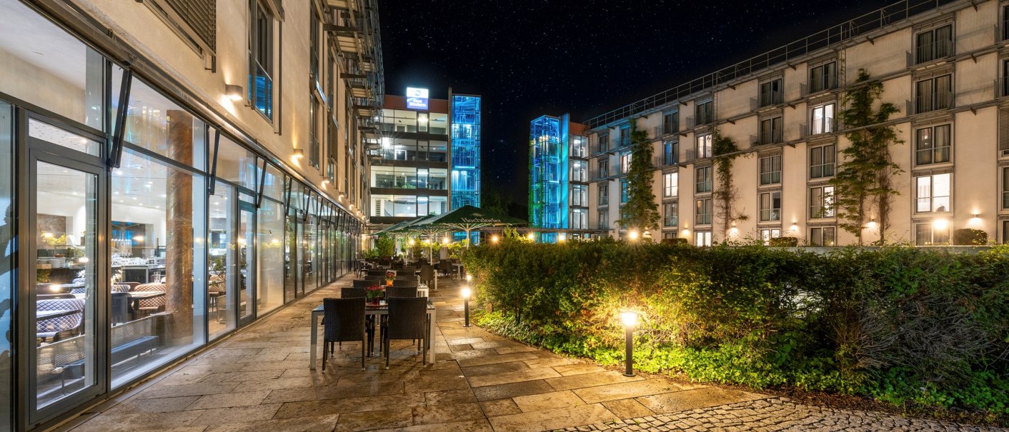 Beleuchteter Hotelhof bei Nacht mit Tischen, Stühlen und umgebenden Gebäuden mit großen Fenstern., © Plaza Residence Stuttgart-Ditzingen Beleuchteter Hotelhof bei Nacht mit Tischen, Stühlen und umgebenden Gebäuden mit großen Fenstern., © Plaza Residence Stuttgart-Ditzingen