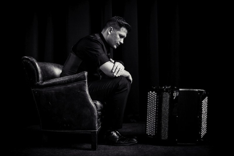 Ein Mann sitzt nachdenklich in einem Sessel neben einem Akkordeon in einem dunklen Raum. Die Szene ist in Schwarz-Wei&szlig; gehalten., &copy; Kulturhaus Schwanen