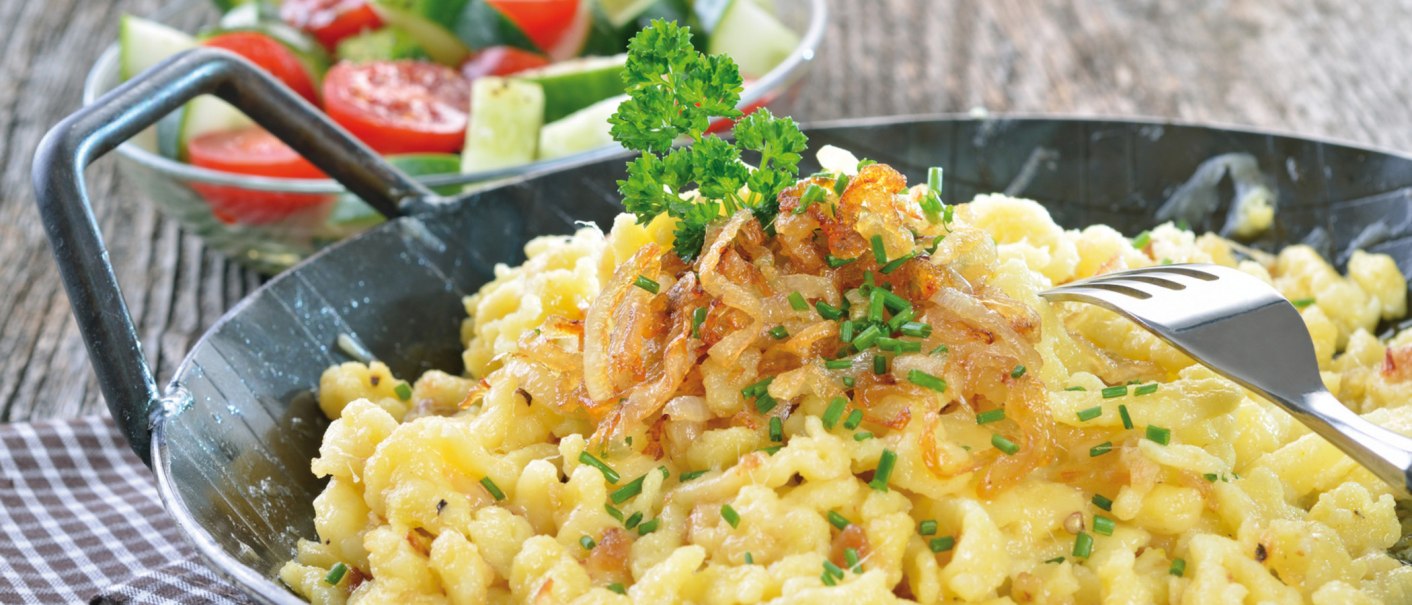 Käsespätzle mit Röstzwiebeln und Schnittlauch in einer Pfanne, daneben ein frischer Salat mit Tomaten und Gurken., © kab-vision - Fotolia Käsespätzle mit Röstzwiebeln und Schnittlauch in einer Pfanne, daneben ein frischer Salat mit Tomaten und Gurken., © kab-vision - Fotolia