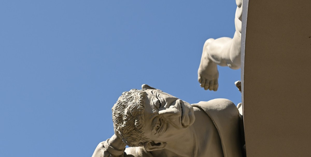 Skulptur eines Mannes, der sich an einem runden Objekt festhält, vor klarem, blauem Himmel., © Bad Urach Tourismus