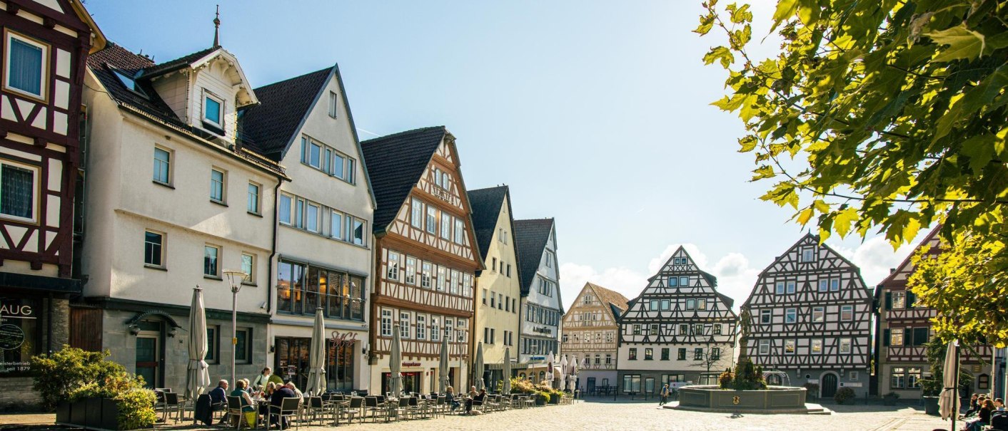 Fachwerkhäuser in der Altstadt von Leonberg. Menschen sitzen an Tischen auf einem sonnigen Platz, umgeben von historischen Gebäuden., © Stuttgart-Marketing GmbH, Sarah Schmid Fachwerkhäuser in der Altstadt von Leonberg. Menschen sitzen an Tischen auf einem sonnigen Platz, umgeben von historischen Gebäuden., © Stuttgart-Marketing GmbH, Sarah Schmid