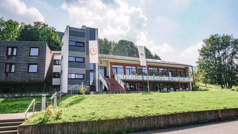 Die Jugendherberge Bad Urach liegt inmitten gr&uuml;ner Natur. Das moderne Geb&auml;ude hat gro&szlig;e Fenster und ist von B&auml;umen umgeben.