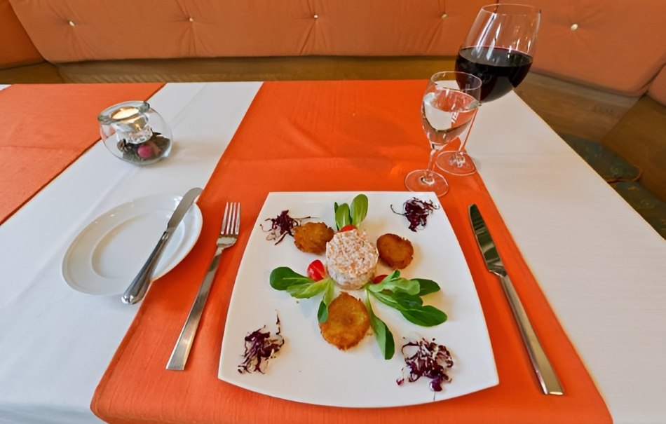 Vorspeise auf weißem Teller mit Salat und Gemüse, dekoriert auf orange-weißer Tischdecke. Ein Glas Rotwein und Wasser stehen daneben., © Hotel Neuwirtshaus