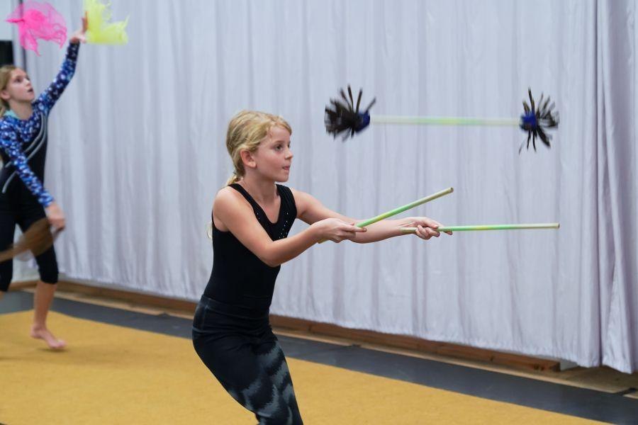 Kinder in einem Zirkus-Workshop jonglieren mit Stäben. Ein Mädchen im Vordergrund konzentriert sich auf ihre Übung. Hintergrund mit Vorhang., © Kunstschule Labyrinth