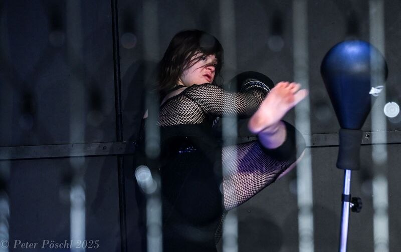 Drei Frauen mit Down-Syndrom tanzen auf einer Bühne. Im Hintergrund ist ein Gitterzaun mit Lichtern und verstreuten Kleidungsstücken zu sehen., © Kulturhaus Schwanen