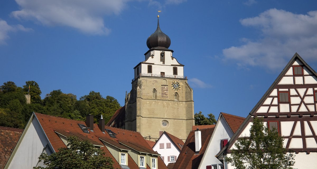 Die Stiftskirche Herrenberg erhebt sich hinter malerischen Fachwerkh&auml;usern unter einem klaren blauen Himmel., &copy; Natur.Nah. Sch&ouml;nbuch & Heckeng&auml;u