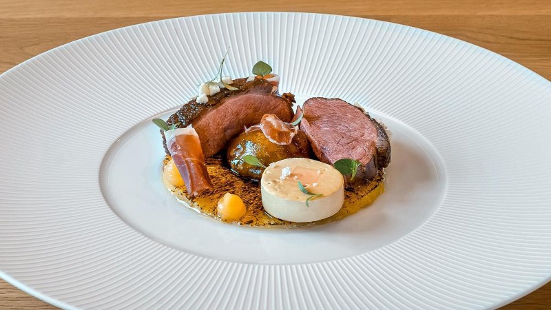 Gourmetgericht mit Entenbrust, dekorativ angerichtet auf einem weißen Teller. Beilagen und Soßen kunstvoll platziert, auf einem Holztisch serviert., © New Josch, Stuttgart Gourmetgericht mit Entenbrust, dekorativ angerichtet auf einem weißen Teller. Beilagen und Soßen kunstvoll platziert, auf einem Holztisch serviert., © New Josch, Stuttgart