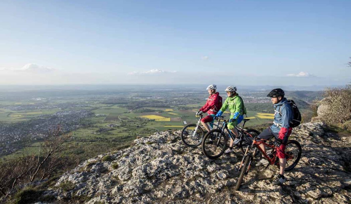 Drei Radfahrer stehen auf einem Felsen und blicken auf die weite Landschaft von Kirchheim unter Teck. Der Himmel ist klar und blau., © Schwäbische Alb Tourismusverband e.V.