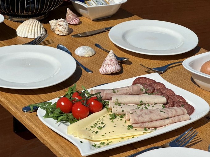 Ein gedeckter Frühstückstisch mit Wurst, Käse, Tomaten und Muscheln als Dekoration., © Cool-Tours StattReisen