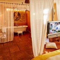 Ein gemütliches Zimmer mit Badewanne, Fernseher und weißen Vorhängen. Der Boden ist aus Terrakottafliesen, ein Sessel steht in der Ecke., © Designhotel & Restaurant Der Zauberlehrling Ein gemütliches Zimmer mit Badewanne, Fernseher und weißen Vorhängen. Der Boden ist aus Terrakottafliesen, ein Sessel steht in der Ecke., © Designhotel & Restaurant Der Zauberlehrling