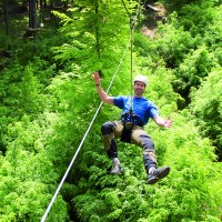 Person mit Helm und Kletterausr&uuml;stung schwebt an einem Seil &uuml;ber einem dichten, gr&uuml;nen Wald im Kletterwald Plochingen., &copy; Sebastian Berger