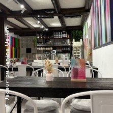 Ein stilvolles Caf&eacute; mit modernen Kunstwerken, wei&szlig;en St&uuml;hlen und dunklen Holztischen. Die Atmosph&auml;re wirkt einladend und kreativ., &copy; links im Bild