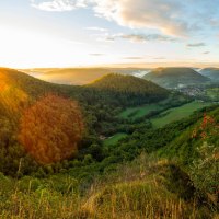 Sonnenaufgang über bewaldeten Hügeln und einem Tal, gesehen vom Badfelsen. Im Vordergrund sind Gräser und Sträucher mit roten Beeren., © Landkreis Göppingen