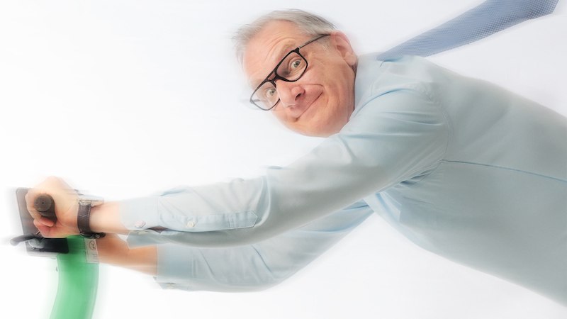 Ein Mann mit Brille und blauer Krawatte h&auml;lt sich an einem gr&uuml;nen E-Scooter fest. Er ist dynamisch zur Seite geneigt, was Bewegung suggeriert., &copy; Mauerwerk GmbH