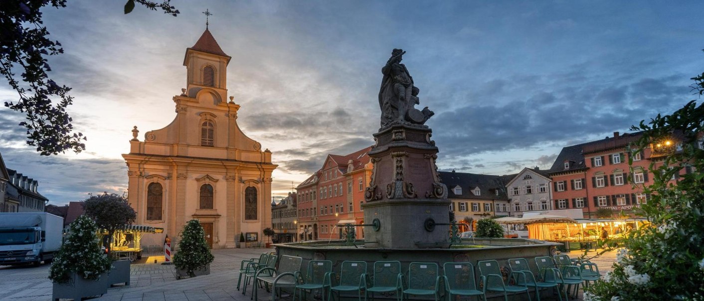 Abendstimmung auf dem Ludwigsburger Marktplatz mit beleuchteter Kirche und Brunnen. Stühle stehen um den Brunnen, Marktstände im Hintergrund., © SMG, Martina Denker Abendstimmung auf dem Ludwigsburger Marktplatz mit beleuchteter Kirche und Brunnen. Stühle stehen um den Brunnen, Marktstände im Hintergrund., © SMG, Martina Denker