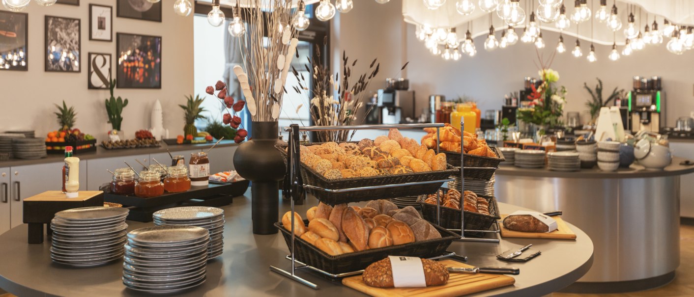 Ein reichhaltiges Frühstücksbuffet mit Brötchen, Croissants und Marmelade in einem stilvoll dekorierten Raum mit modernen Leuchten., © Novum Management GmbH Ein reichhaltiges Frühstücksbuffet mit Brötchen, Croissants und Marmelade in einem stilvoll dekorierten Raum mit modernen Leuchten., © Novum Management GmbH