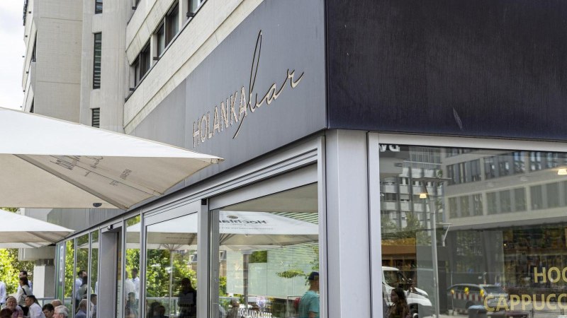 Au&szlig;enansicht der Holanka Bar mit gro&szlig;en Sonnenschirmen. Menschen sitzen und stehen im Au&szlig;enbereich. Moderne Geb&auml;ude im Hintergrund., &copy; SMG, Sarah Schmid