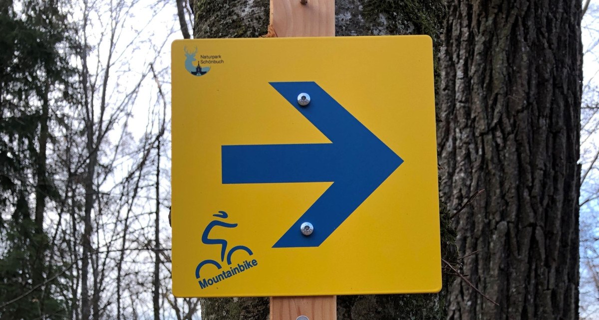 Ein gelbes Schild mit blauem Pfeil und Mountainbike-Symbol im Naturpark Sch&ouml;nbuch weist den Weg., &copy; Natur.Nah. Sch&ouml;nbuch & Heckeng&auml;u