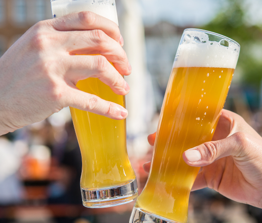 Zwei Personen sto&szlig;en mit gef&uuml;llten Weizengl&auml;sern an, im Hintergrund ein sonniger Biergarten., &copy; Ludwigsburg