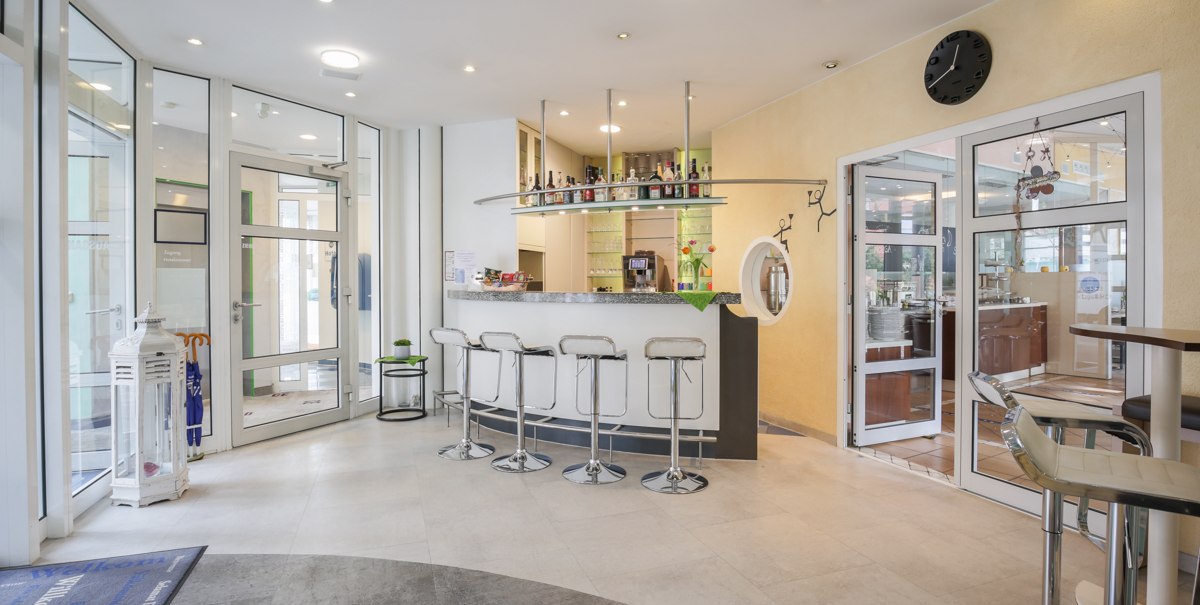 Moderne Hotelbar mit weißen Barhockern, einer Theke mit Flaschen und Gläsern. Glastüren führen zu einem weiteren Raum. Helle, einladende Atmosphäre., © TOMAS Moderne Hotelbar mit weißen Barhockern, einer Theke mit Flaschen und Gläsern. Glastüren führen zu einem weiteren Raum. Helle, einladende Atmosphäre., © TOMAS