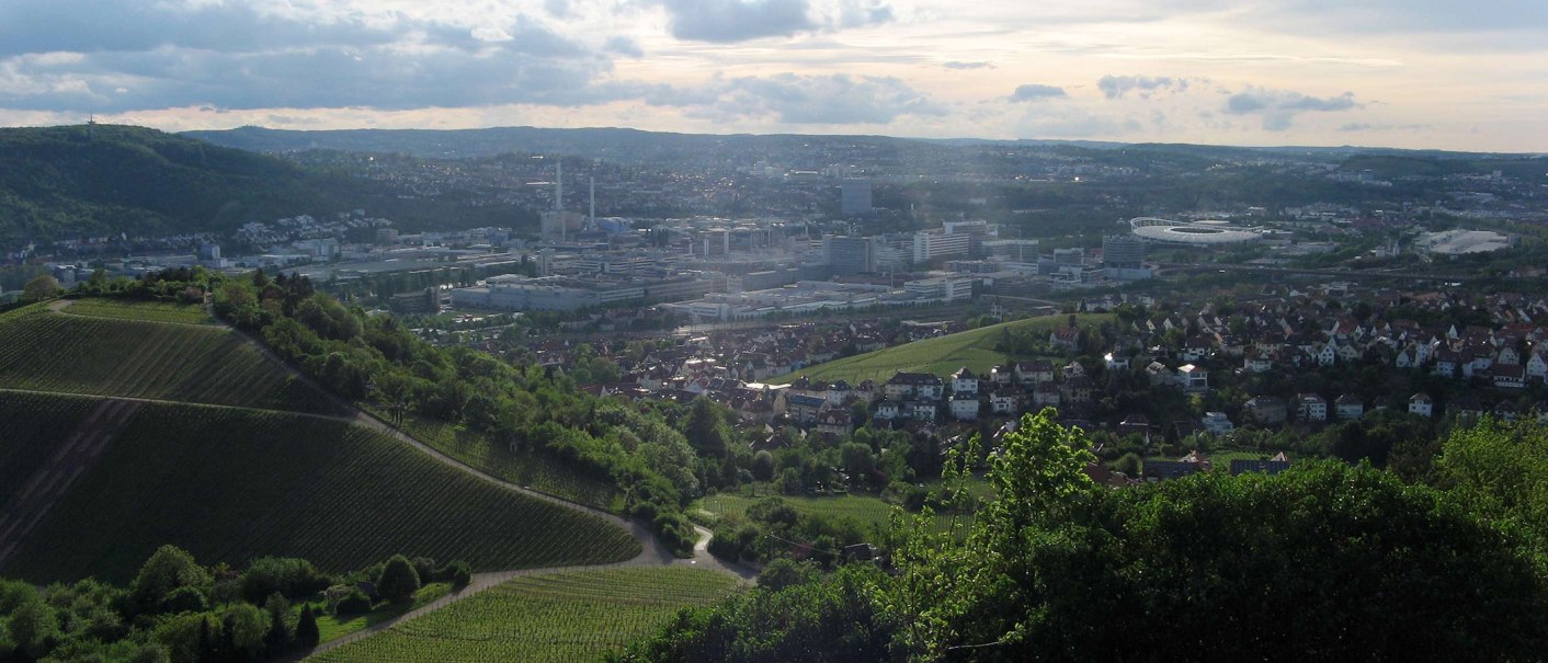 Panoramablick auf Untertürkheim: Weinberge im Vordergrund, Stadt und Industriegebäude im Hintergrund unter bewölktem Himmel., © Stuttgart-Marketing GmbH