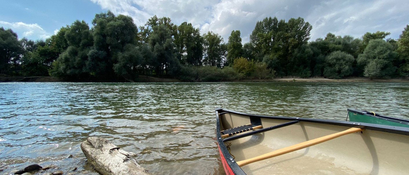 Ein Kanu liegt am Ufer eines ruhigen Flusses, umgeben von dichtem Wald und bewölktem Himmel., © Manuel Mattern Ein Kanu liegt am Ufer eines ruhigen Flusses, umgeben von dichtem Wald und bewölktem Himmel., © Manuel Mattern