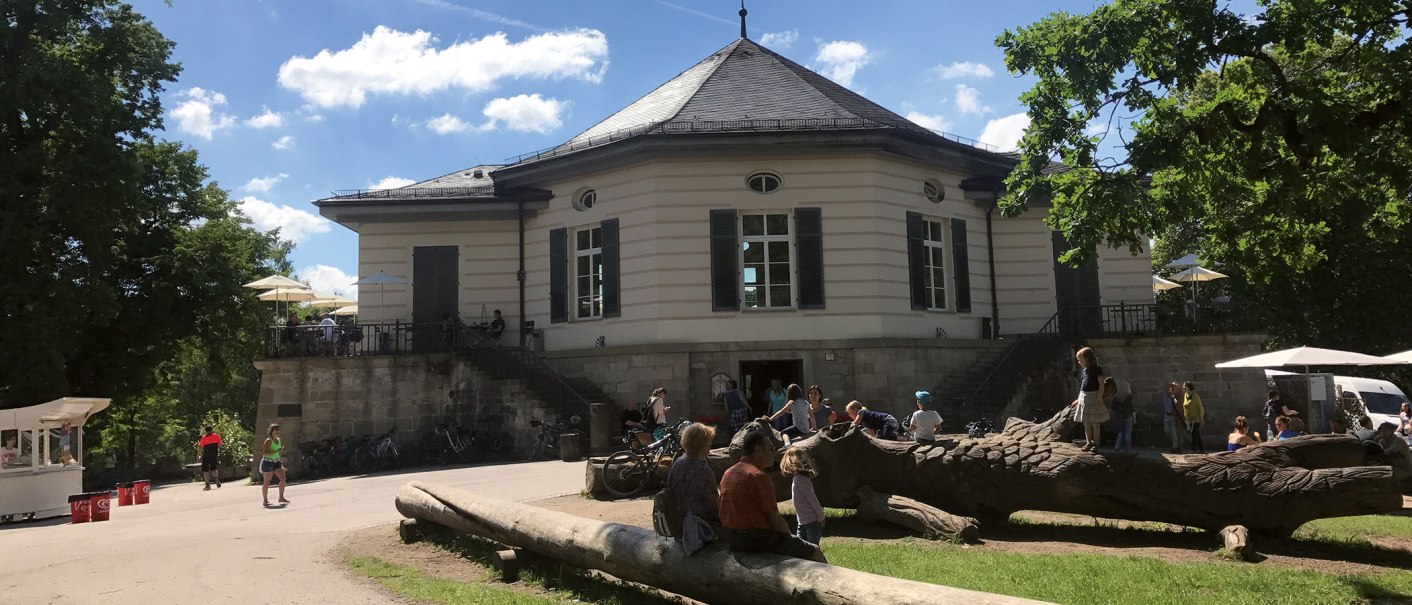 Das Bärenschlössle in Stuttgart, umgeben von Bäumen, mit Menschen, die draußen bei sonnigem Wetter entspannen und spielen., © SMG Das Bärenschlössle in Stuttgart, umgeben von Bäumen, mit Menschen, die draußen bei sonnigem Wetter entspannen und spielen., © SMG