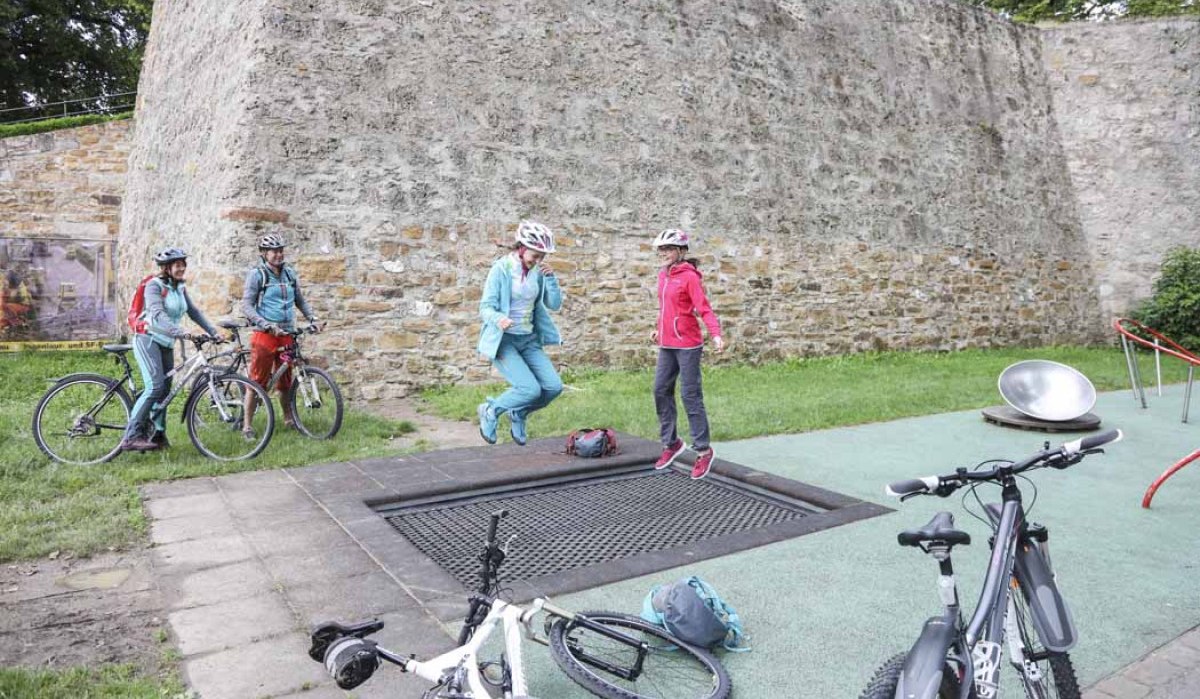 Zwei Personen springen auf einem Trampolin, während zwei andere mit Fahrrädern zuschauen. Im Hintergrund eine hohe Steinmauer., © Schwäbische Alb Tourismusverband e.V. Zwei Personen springen auf einem Trampolin, während zwei andere mit Fahrrädern zuschauen. Im Hintergrund eine hohe Steinmauer., © Schwäbische Alb Tourismusverband e.V.