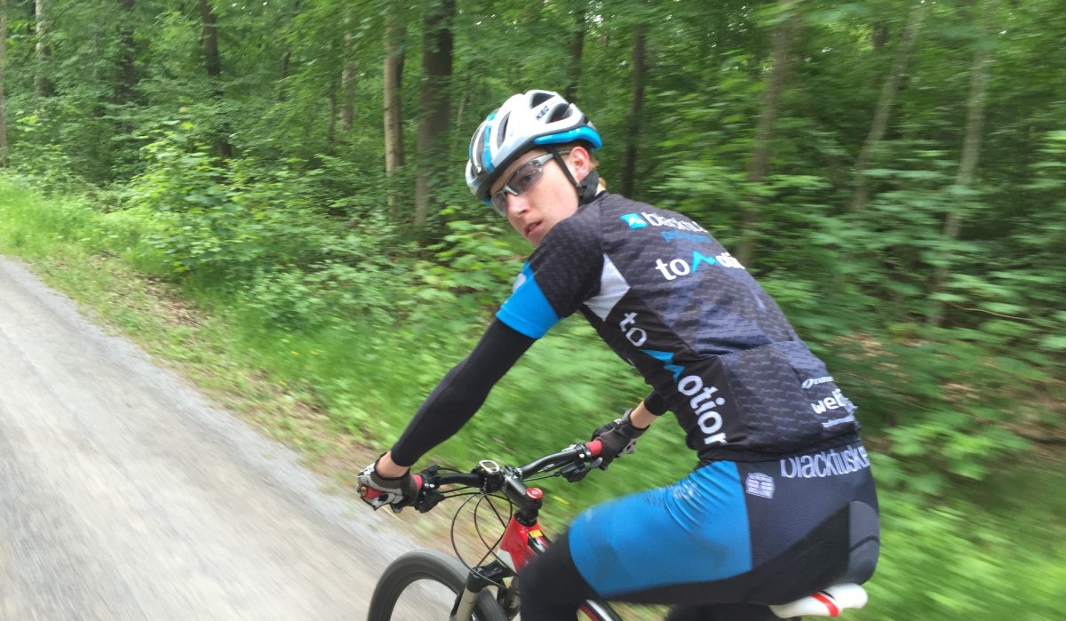 Ein Radfahrer mit Helm und Sportkleidung fährt auf einem Schotterweg durch einen grünen Wald., © www.pro-cycl.de