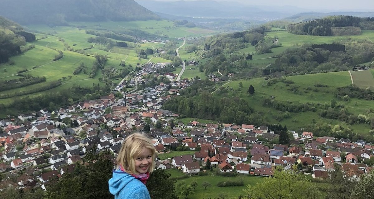 Ein Kind in blauer Jacke steht auf einem Felsen und blickt auf ein Dorf in einer gr&uuml;nen H&uuml;gellandschaft., &copy; Touristik und Marketing GmbH