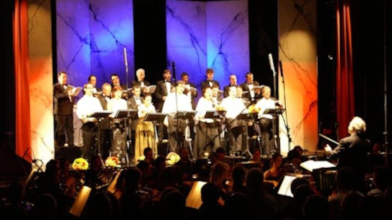 Ein Chor und Orchester f&uuml;hren ein Konzert auf. Die B&uuml;hne ist in Blau und Rot beleuchtet, der Dirigent steht vor dem Orchester., &copy; Touristik Bad Wildbad GmbH