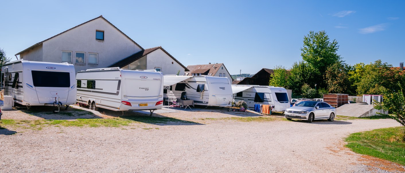 Wohnmobilstellplatz mit mehreren Wohnwagen und einem Auto. Im Hintergrund sind Häuser und Bäume zu sehen. Der Himmel ist klar und blau., © Stuttgart-Marketing GmbH, Thomas Niedermüller