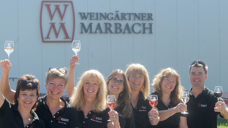 Sieben Personen heben lächelnd Weingläser vor einem Gebäude mit 'Weingärtner Marbach'-Logo., © Weingärtner Marbach e. G. Sieben Personen heben lächelnd Weingläser vor einem Gebäude mit 'Weingärtner Marbach'-Logo., © Weingärtner Marbach e. G.