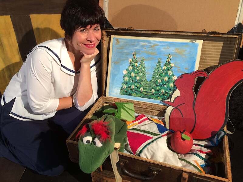 Frau in Matrosenhemd neben einem offenen Koffer mit Weihnachtsbild, Stofftier und Dekorationen. Der Koffer enthält ein Bild von Tannenbäumen., © Stadtverwaltung Vaihingen an der Enz Frau in Matrosenhemd neben einem offenen Koffer mit Weihnachtsbild, Stofftier und Dekorationen. Der Koffer enthält ein Bild von Tannenbäumen., © Stadtverwaltung Vaihingen an der Enz