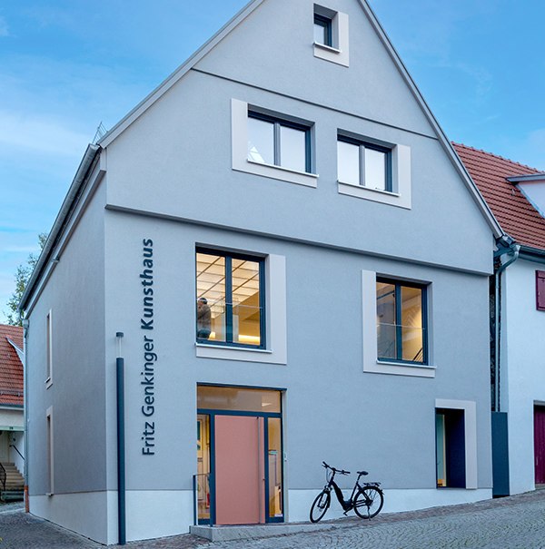 Das Fritz Genkinger Kunsthaus hat eine graue Fassade mit großen Fenstern. Ein Fahrrad steht davor auf dem gepflasterten Weg., © Freundeskreis Fritz Genkinger e.V. Das Fritz Genkinger Kunsthaus hat eine graue Fassade mit großen Fenstern. Ein Fahrrad steht davor auf dem gepflasterten Weg., © Freundeskreis Fritz Genkinger e.V.