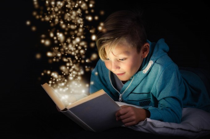 Ein Kind in einem blauen Hoodie liest ein Buch, aus dem funkelnde Lichter aufsteigen, vor schwarzem Hintergrund., &copy; Stadt N&uuml;rtingen