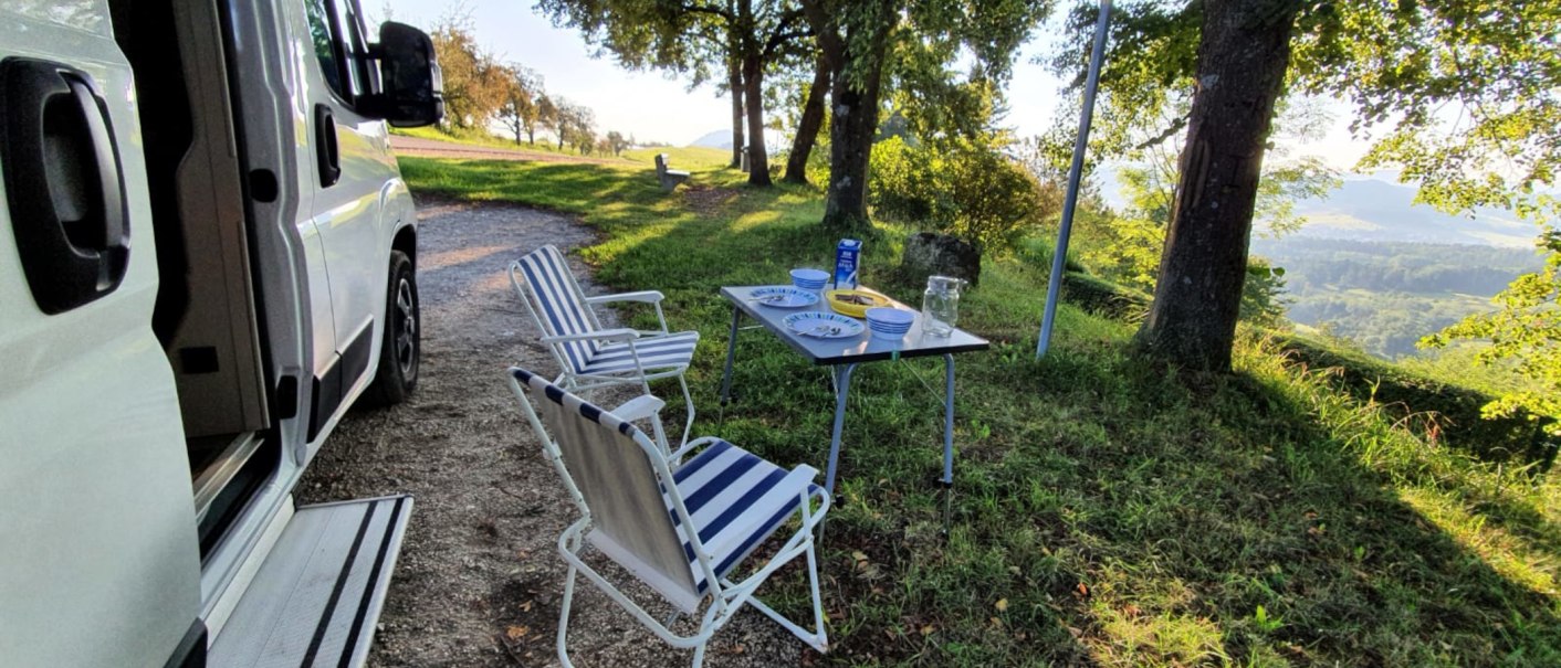 Wohnmobilstellplatz mit Tisch und Stühlen im Grünen. Teller und Gläser auf dem Tisch, umgeben von Bäumen und mit Blick auf die Landschaft., © Stadtmarketing Göppingen