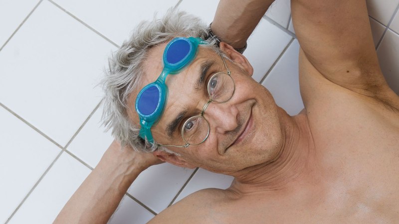 Ein lächelnder Mann mit Schwimmbrille und Brille liegt auf weißen Fliesen. Er hat graue Haare und wirkt entspannt., © Martin Herrmann Ein lächelnder Mann mit Schwimmbrille und Brille liegt auf weißen Fliesen. Er hat graue Haare und wirkt entspannt., © Martin Herrmann