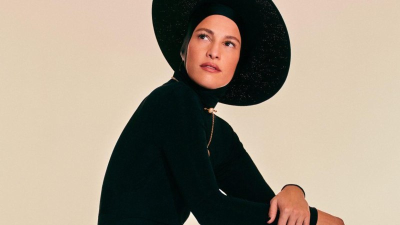 Eine Person in einem eleganten schwarzen Outfit mit gro&szlig;em Hut sitzt und blickt nachdenklich zur Seite., &copy; Carminho &copy; Fernando Tomaz