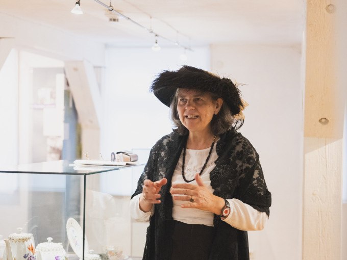 Eine Frau in historischer Kleidung steht in einem Museum neben einer Vitrine mit Porzellan. Sie tr&auml;gt einen schwarzen Hut und eine Spitzenjacke., &copy; Eigenbetrieb Tourismus und Citymanagement Schorndorf