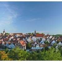 Panorama einer Stadt mit vielen Fachwerkhäusern und Kirchtürmen, umgeben von grünen Bäumen, unter einem klaren blauen Himmel., © Stadtverwaltung Marbach am Neckar