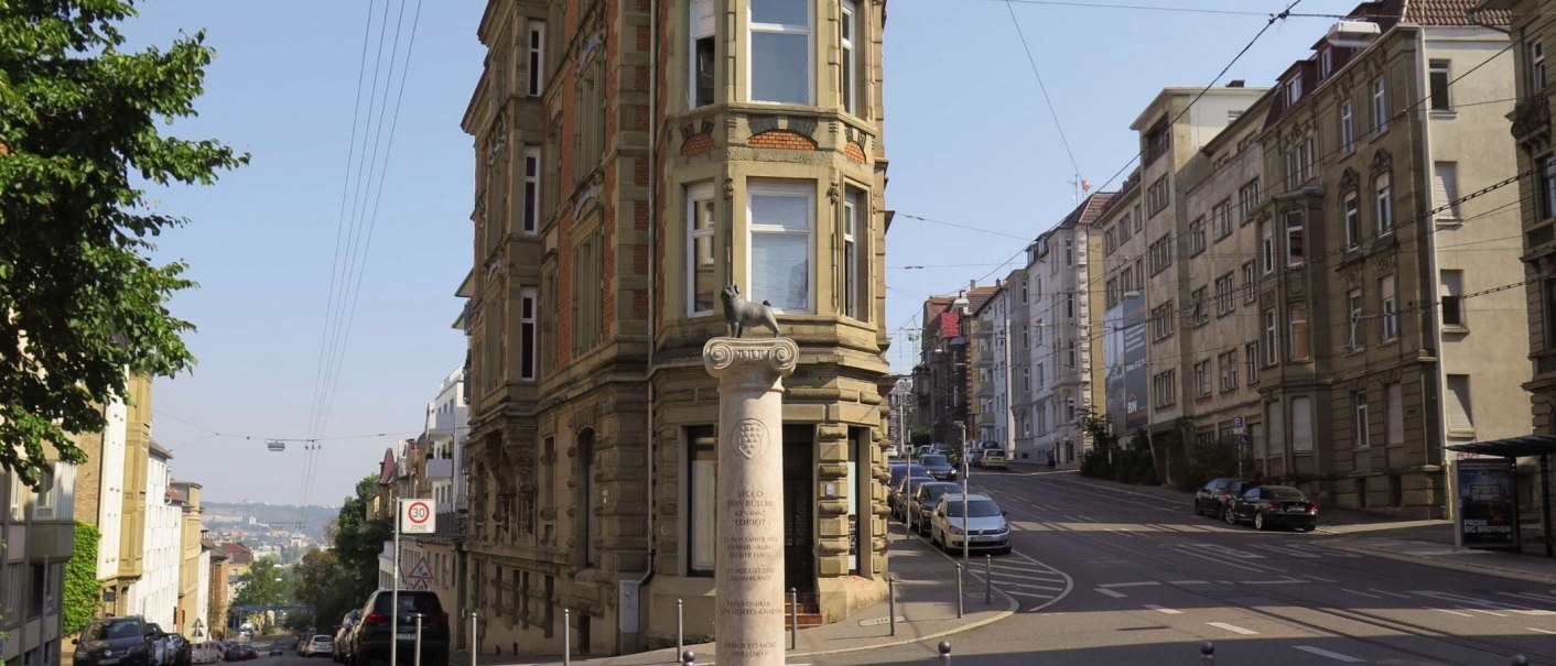 Das Loriot-Denkmal am Eugensplatz in Stuttgart zeigt eine S&auml;ule mit einer Skulptur darauf. Im Hintergrund sind historische Geb&auml;ude und eine Stra&szlig;e zu sehen., &copy; Stuttgart-Marketing GmbH