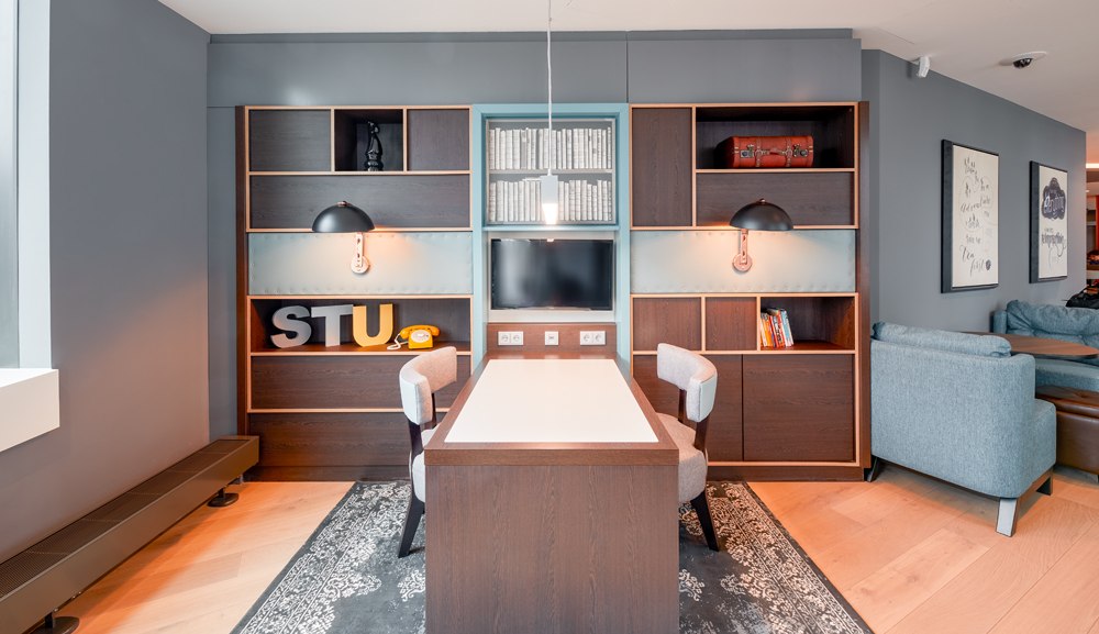 Moderner Arbeitsbereich mit Tisch, Regalen, Dekorationen und gemütlichen Sesseln in einem stilvollen Raum., © Premier Inn