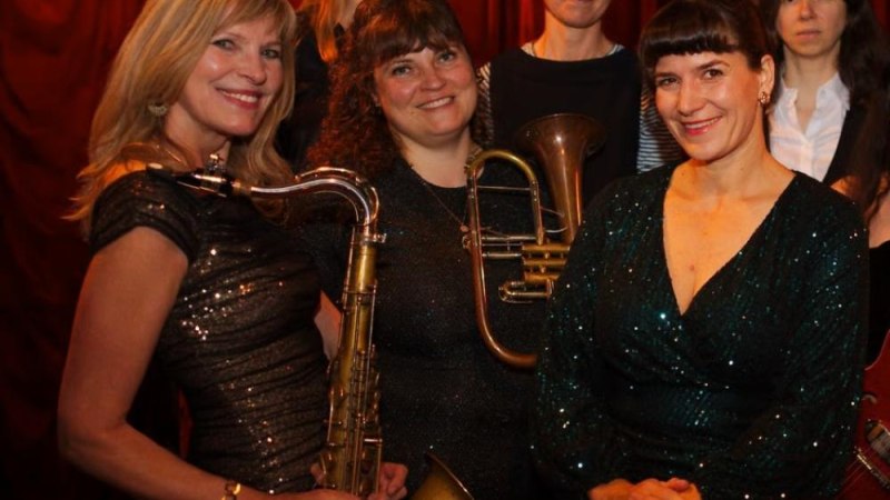 Sechs Frauen posieren mit Musikinstrumenten vor einem roten Vorhang. Sie tragen elegante, glitzernde Kleidung und l&auml;cheln in die Kamera., &copy; Foto Women in Swing
