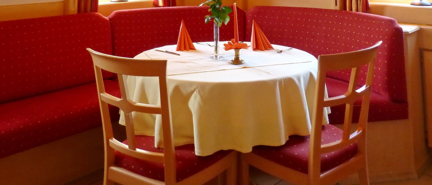 Gemütliche Restaurant-Ecke mit rundem Tisch, weißer Tischdecke, roten Stühlen und Vorhängen. Eine Vase mit Blumen steht auf dem Tisch., © Hotel & Restaurant Sonne