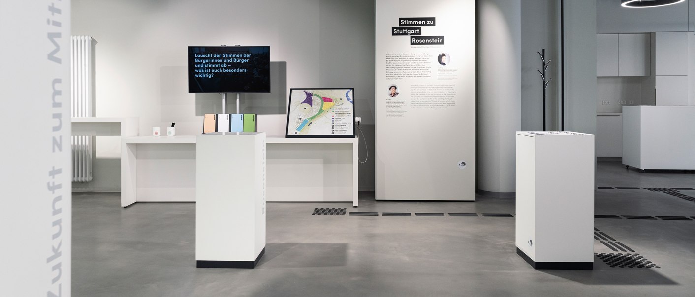 Moderne Ausstellung mit weißen Podesten, Infotafeln und einem Bildschirm. Thema: Stimmen zu Stuttgart Rosenstein. Minimalistisches Design., © Stadt Stuttgart / Dominique Brewing