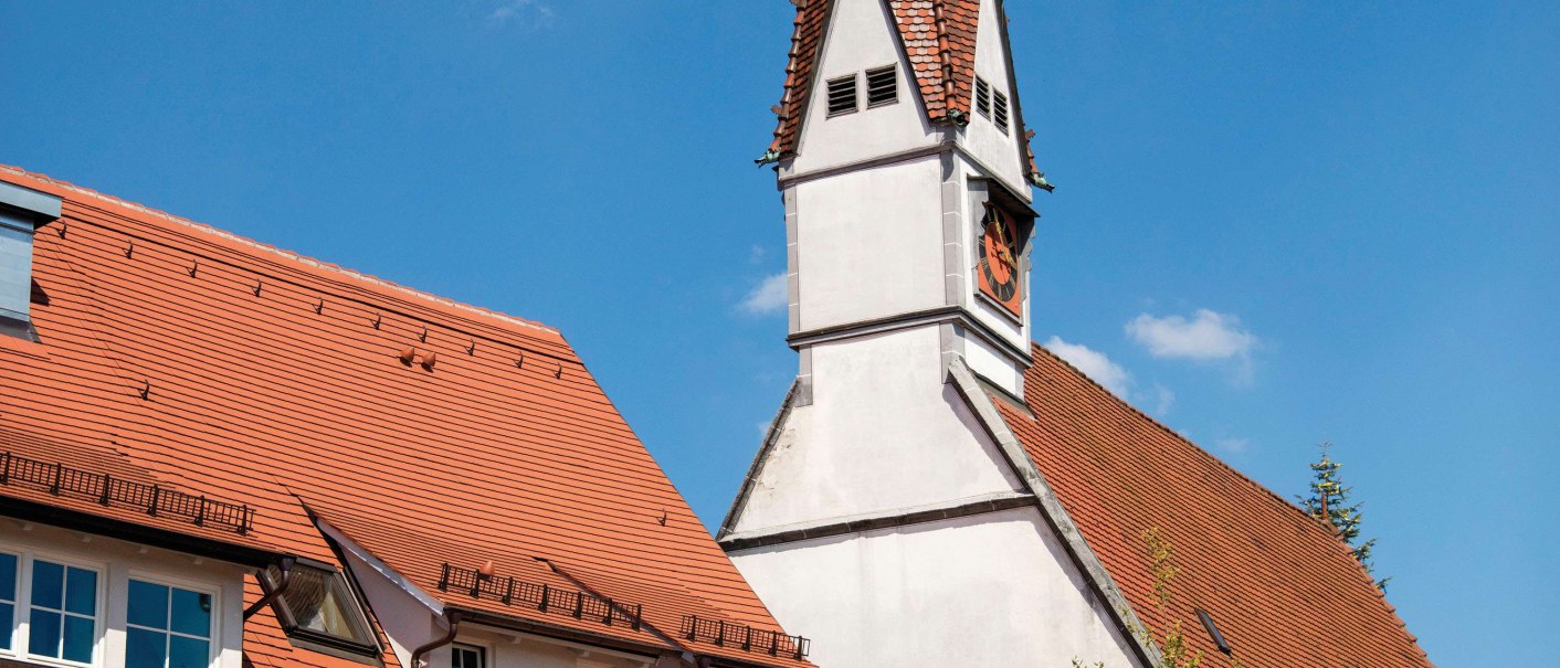 Bunt bemaltes Gebäude mit Drachenmotiv und pinken Details neben einer Kirche mit spitzem Turm in Plochingen., © Stuttgart-Marketing GmbH, Achim Mende