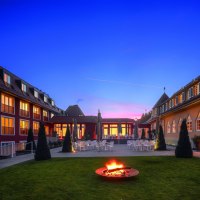 Das Waldhotel Stuttgart bei D&auml;mmerung, mit beleuchteten Fenstern und einer Feuerstelle im Garten. Der Himmel ist blau mit einem rosa Streifen., &copy; Waldhotel Stuttgart GmbH